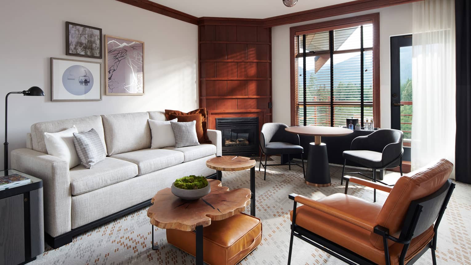 Living room with cream couch, wooden nesting tables, brown leather accent chair, window with view of foliage