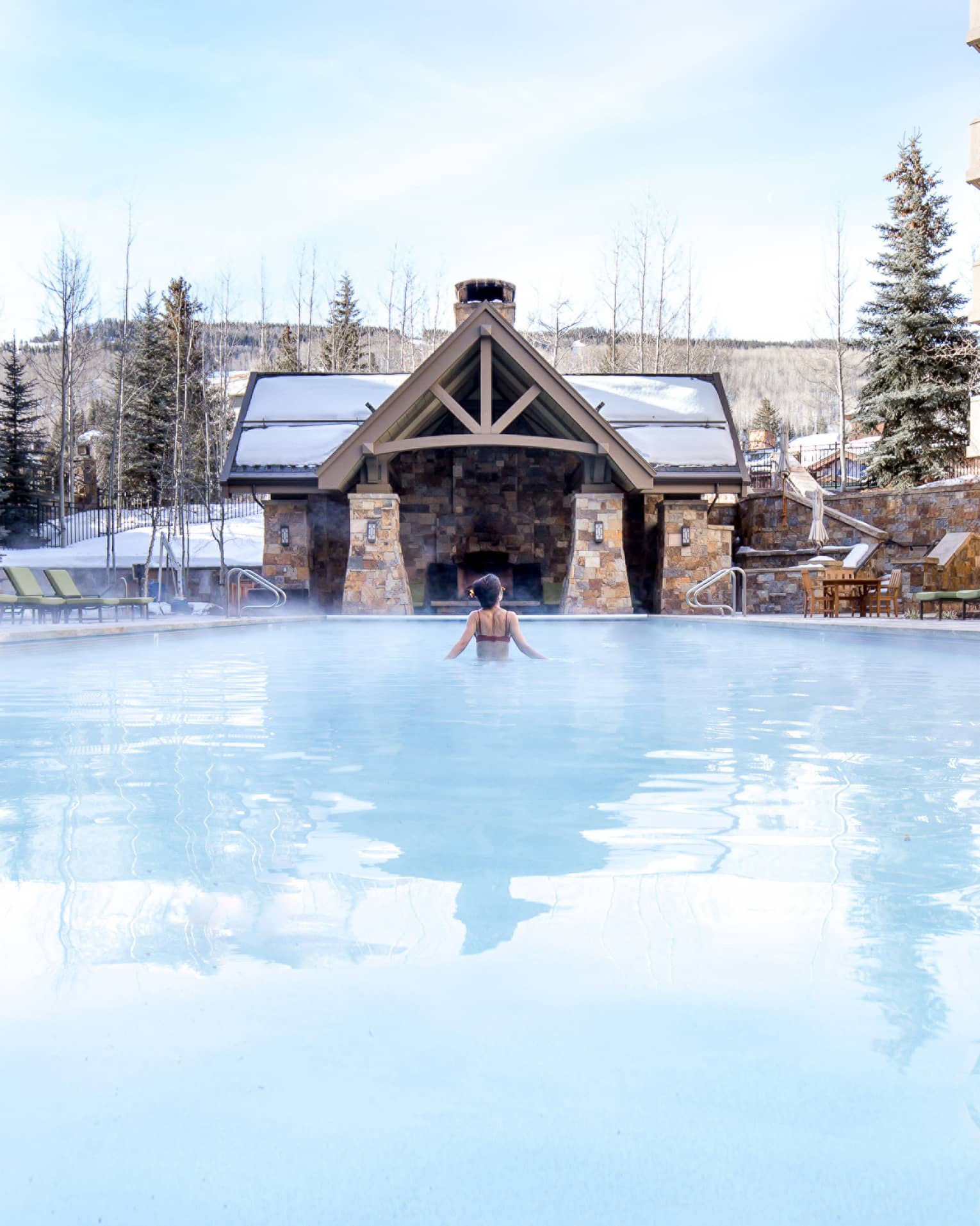 A woman in a pool with trees covered in snow around her.