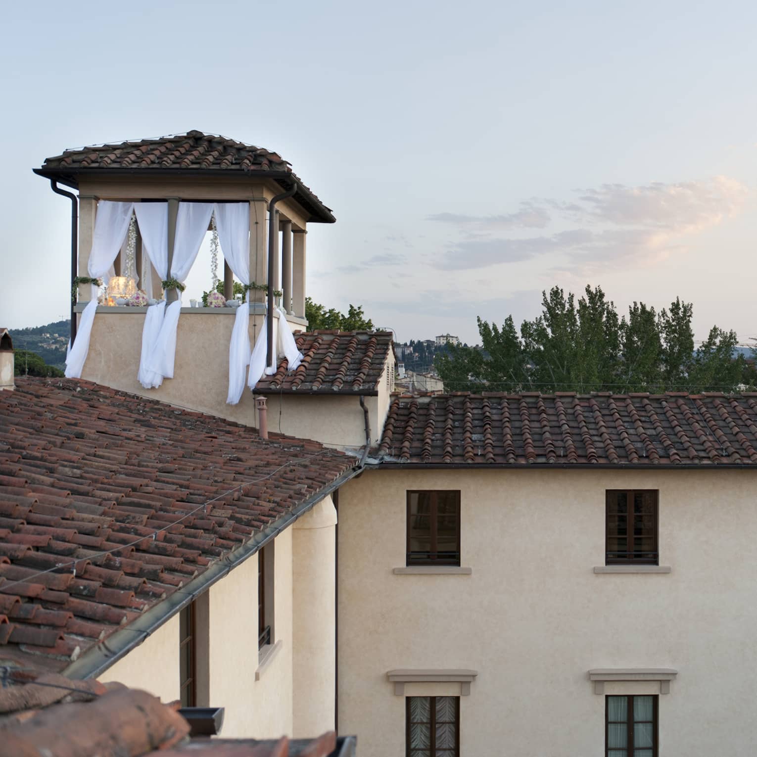 Looking across the red tiled rooftop of the Hotel to a small terrace with white flowing curtains and romantic decorations.