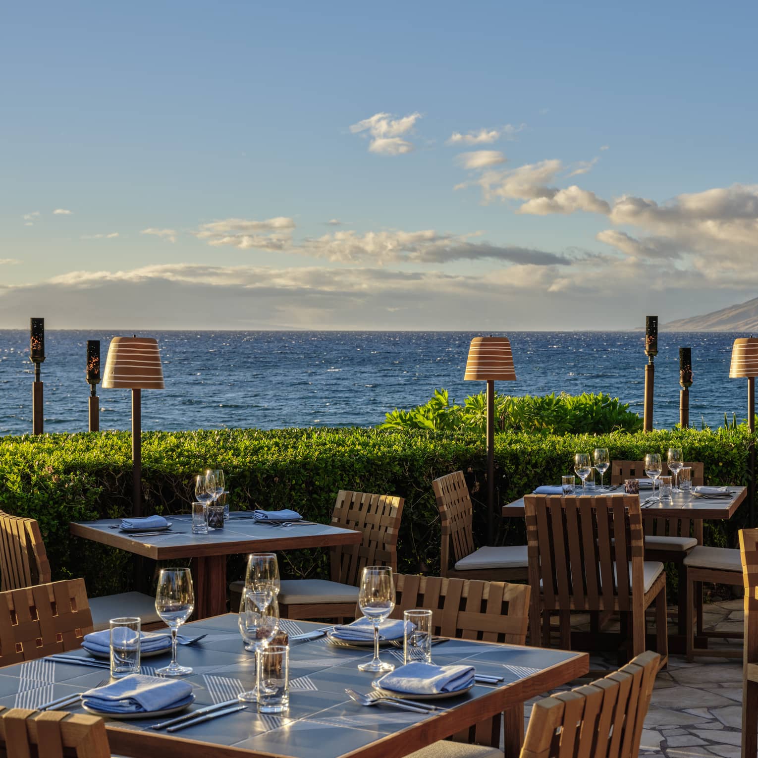 Oceanfront outdoor dining area with wooden tables and chairs set for service
