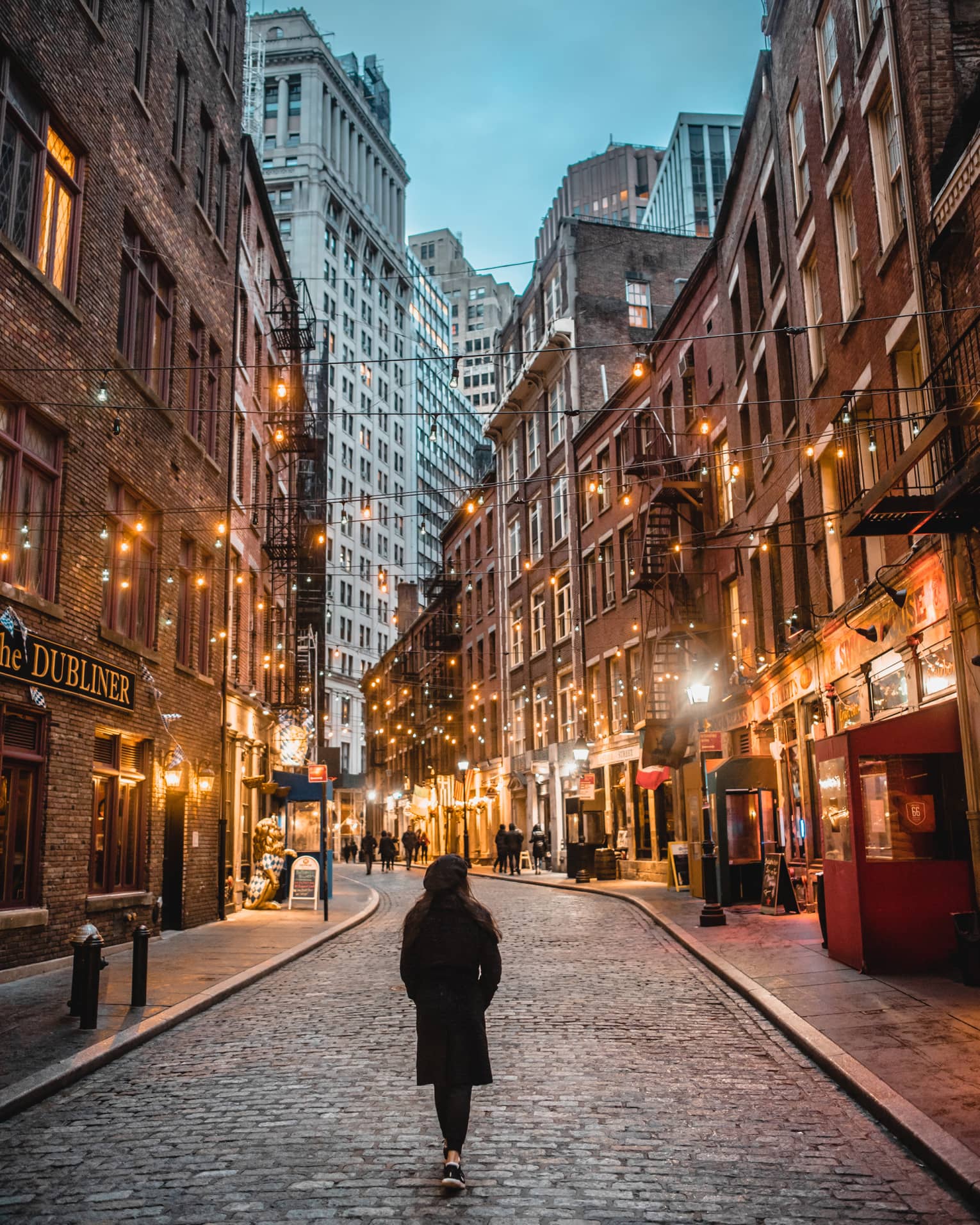A woman in a winter coat walking down a street with many lights.