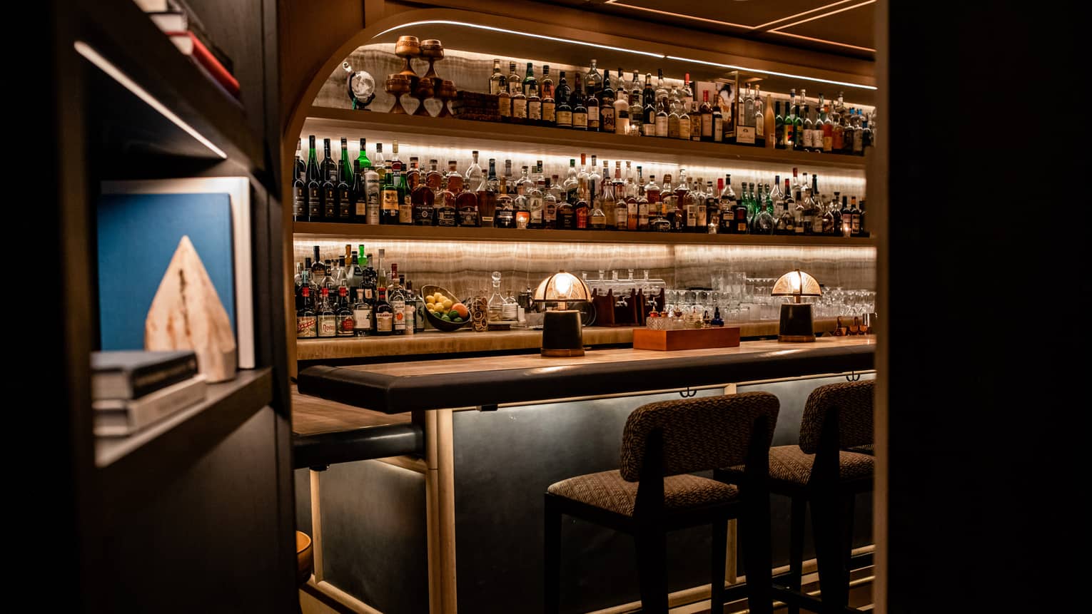 A bar with many bottles of liquor behind a bookcase.