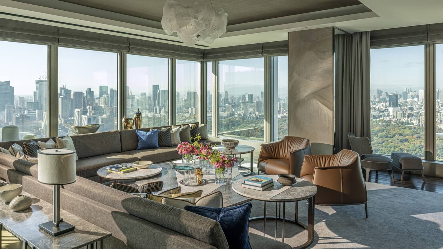 Luxury imperial hotel suite with large sectional sofa, leather armchairs, multiple coffee tables and floor-to-ceiling windows with panoramic city views