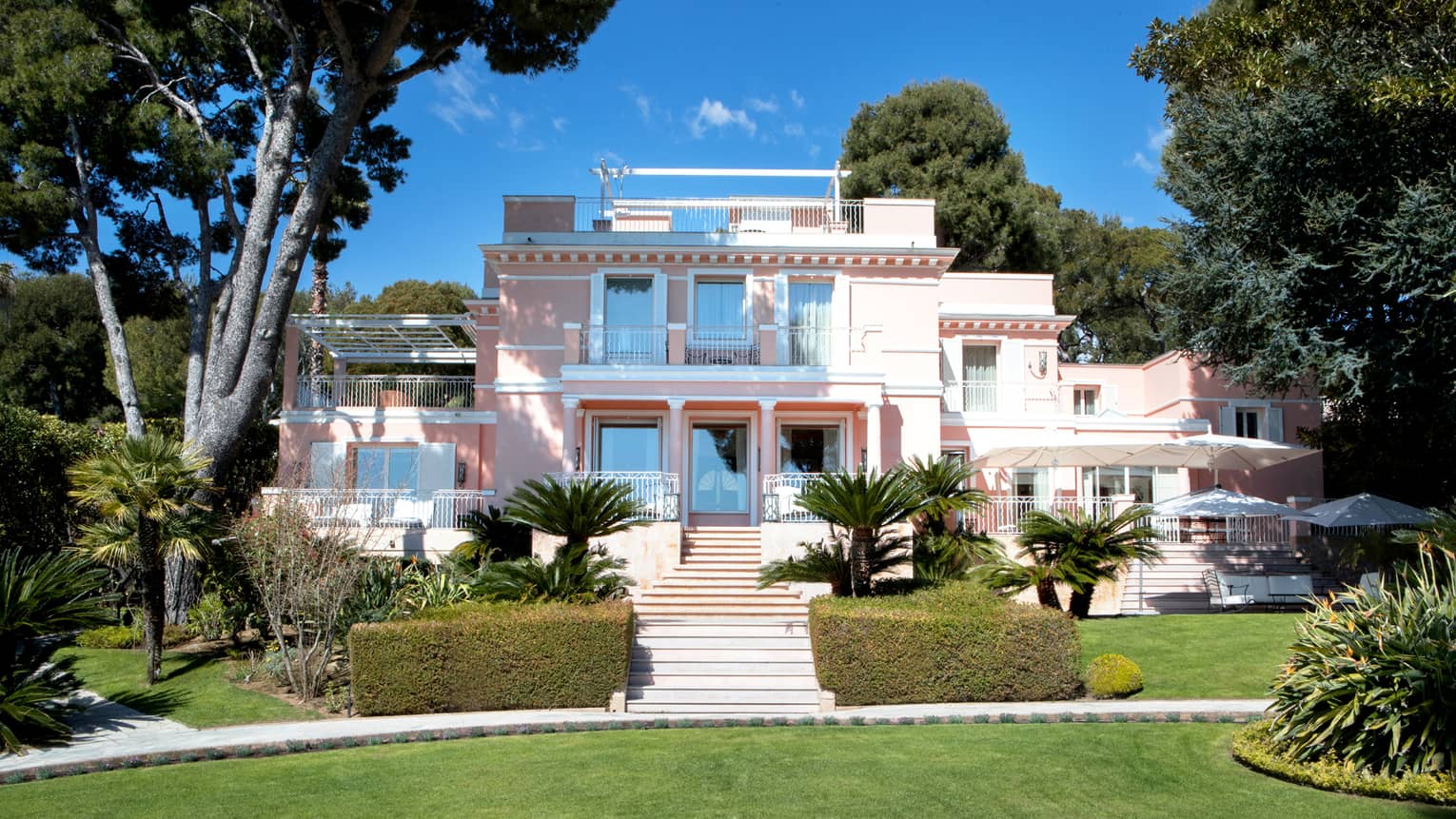 Manicured gardens, steps up to large three-storey pink Villa Rose-Pierre