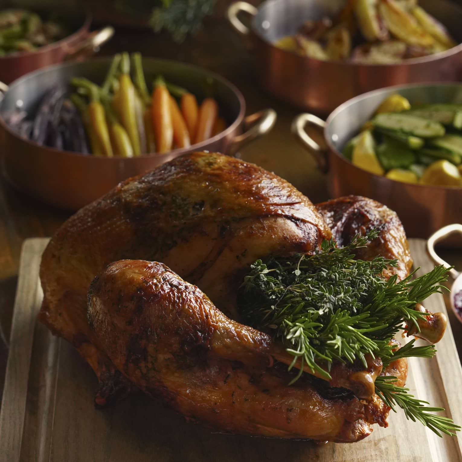 Festive turkey stuffed with rosemary on carving board, accompaniments and side dishes in the background