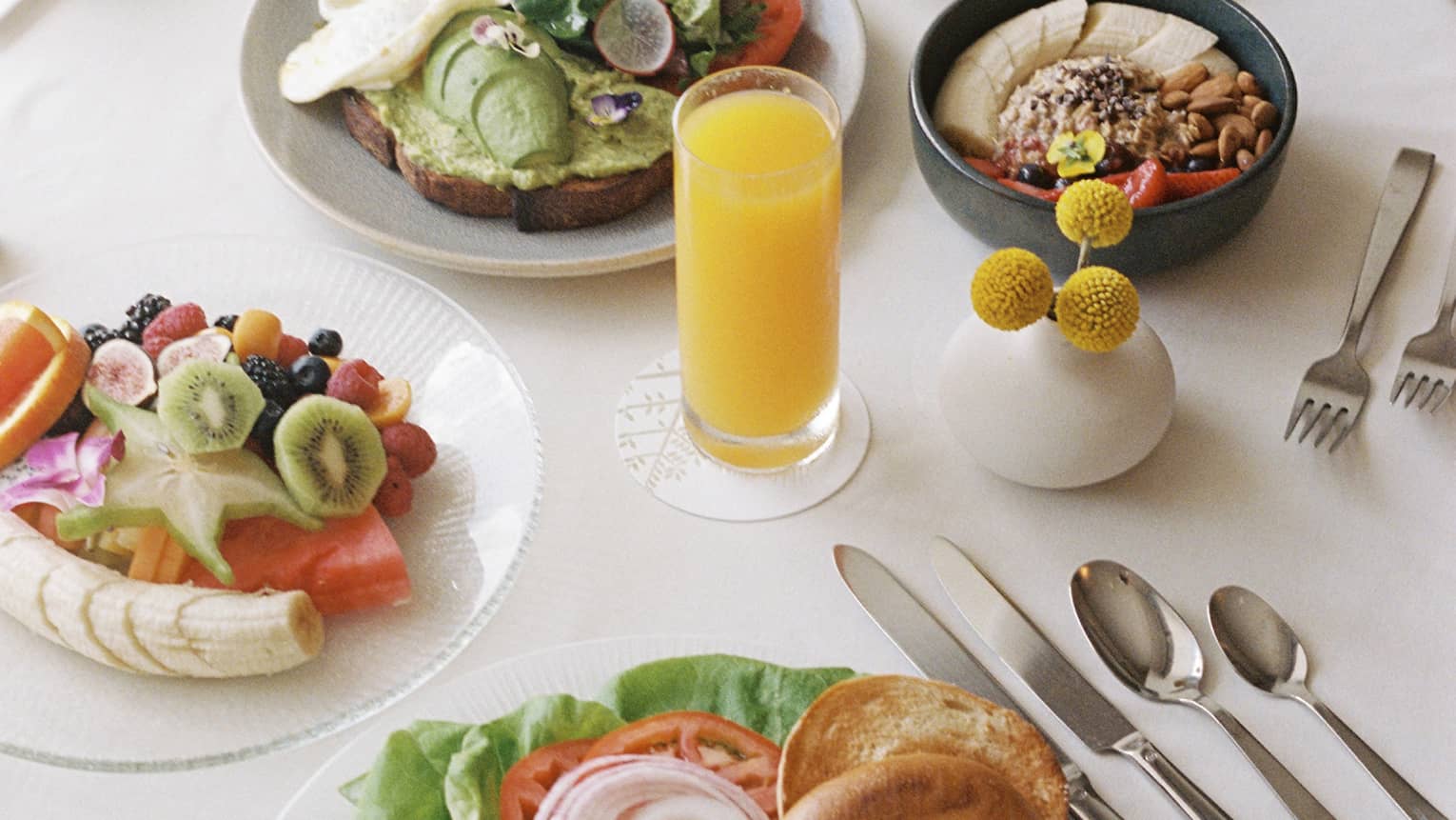 Dining table with plates of food and fruit and utensils set beside the plates.