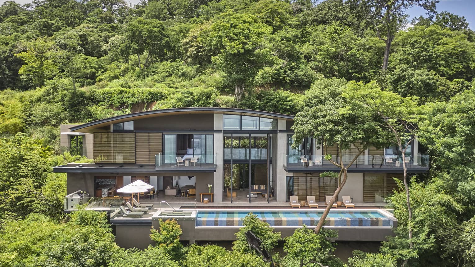 Exterior of private villa nestled in the trees with long rectangular pool