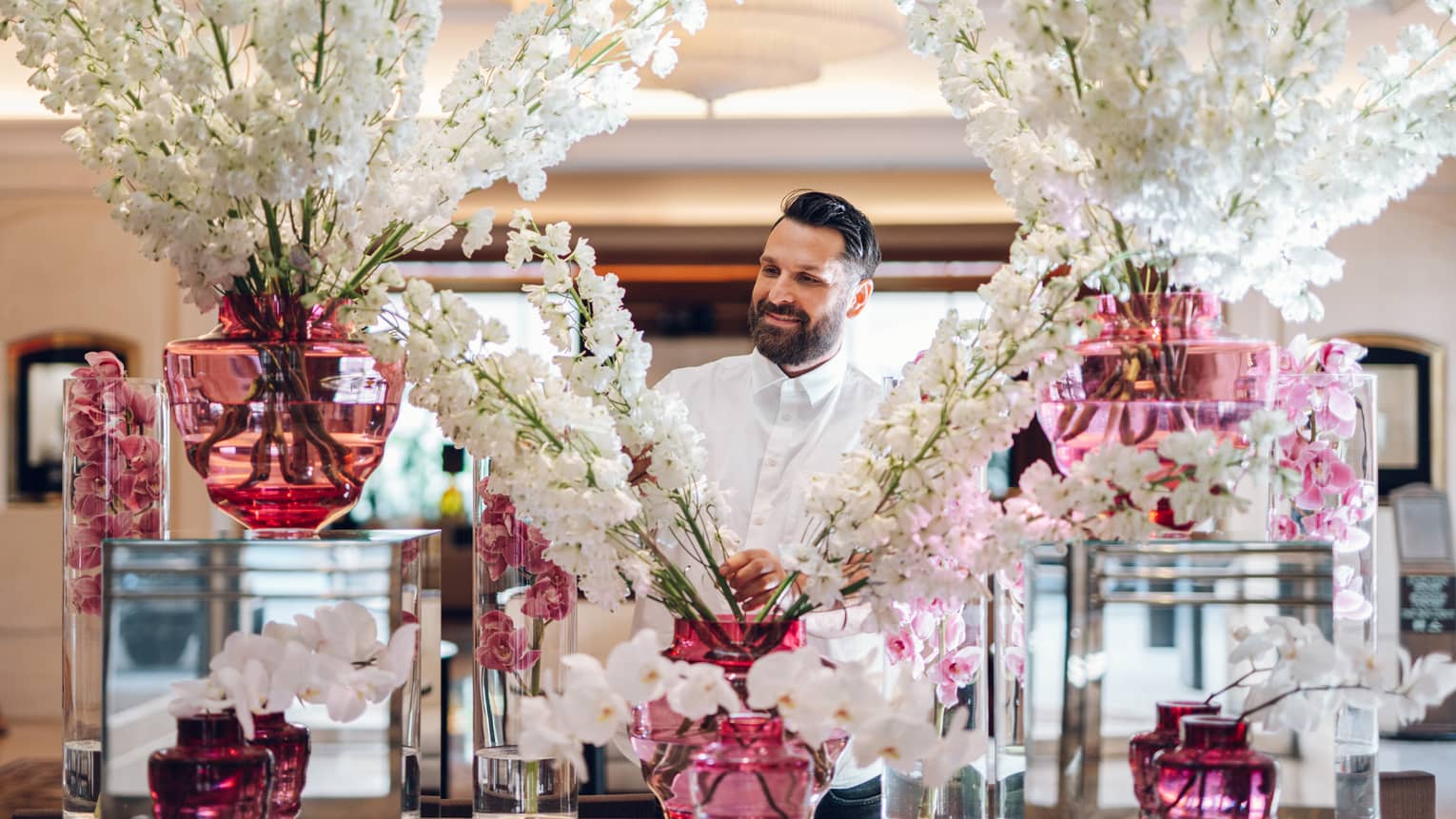Floral designer standing behind large display of white flower sprays in assorted pink vases