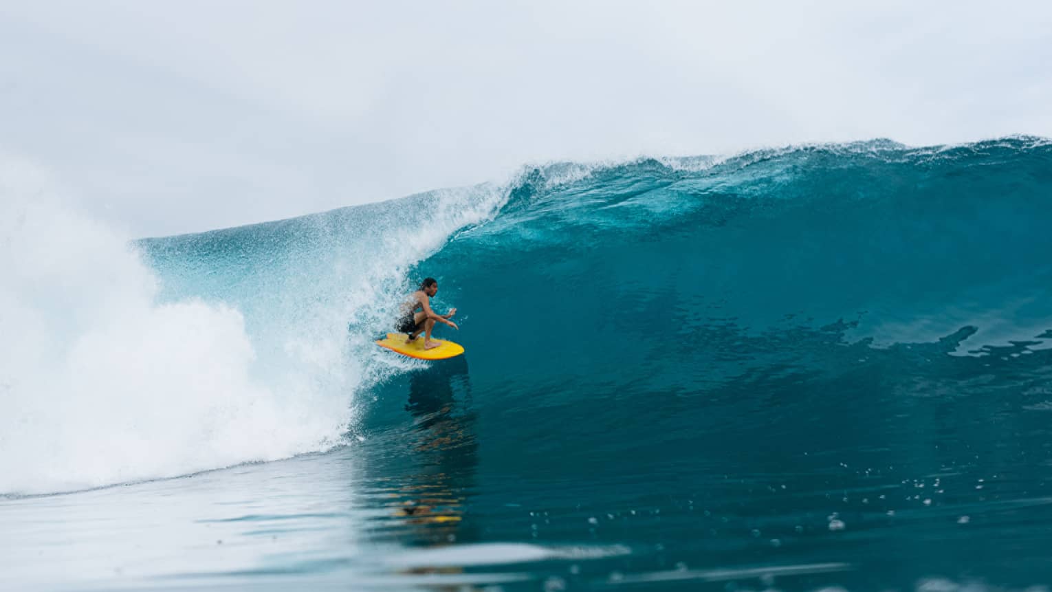 Person on yellow surfboard ducks underneath wave in the middle of the ocean