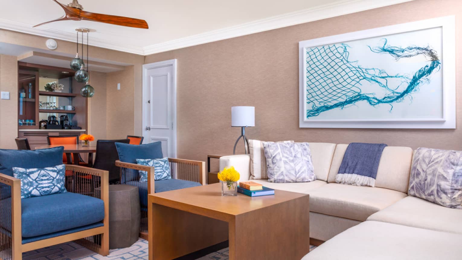 Modern living room with sectional sofa, blue armchairs, abstract art and view of dining area and bar in background