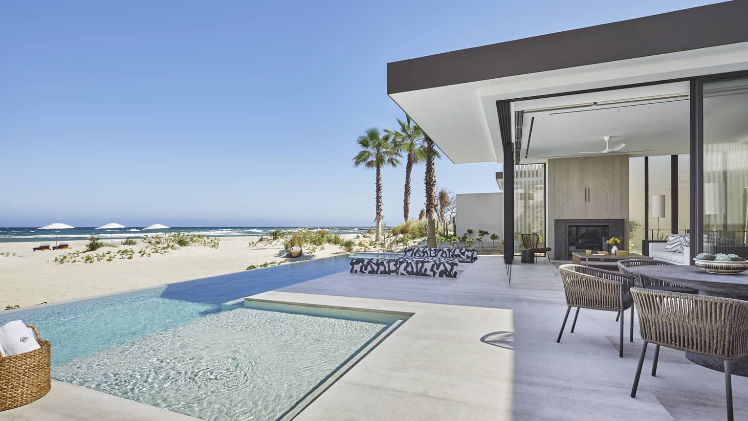 Beside an indoor-outdoor patio, a clear infinity pool overlooks a grassy beach and the breaking waves of the ocean beyond.