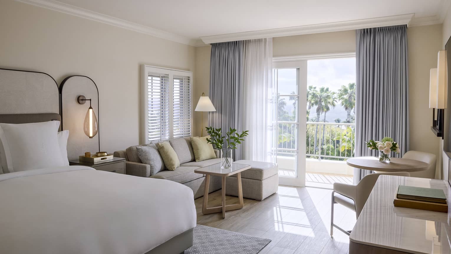 Elegant residential room with king bed, sitting area with sofa, table with two chairs, and balcony