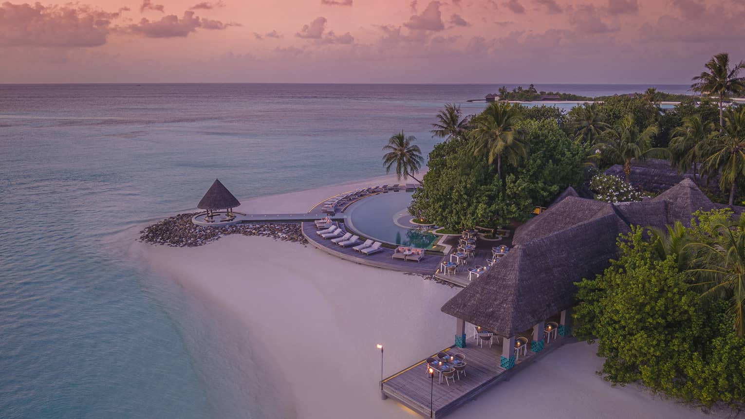Aerial view of beachfront straw roof pavilion at sunset