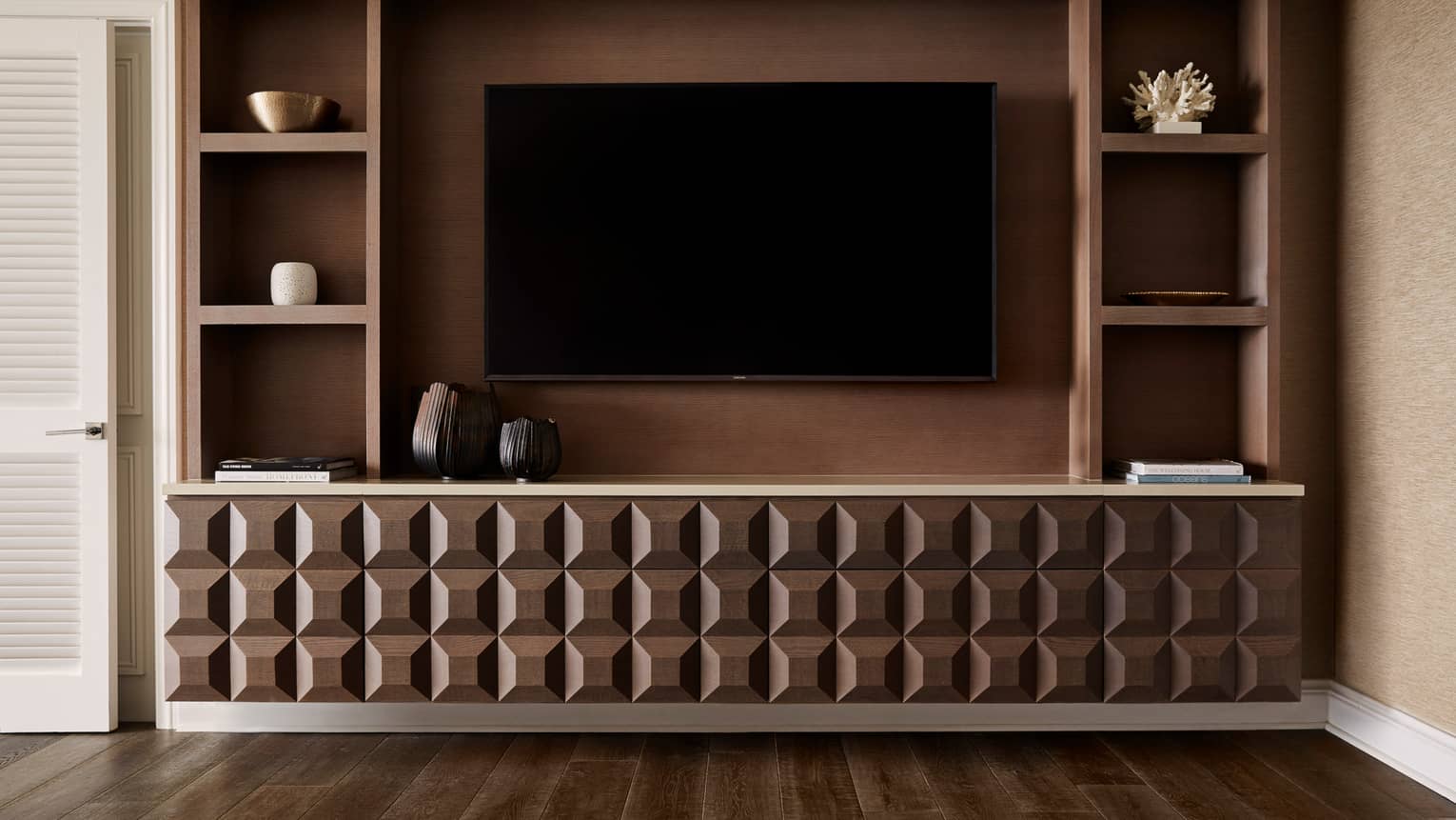 Wall-mounted TV with geometric wood cabinet and built-in shelves displaying decor items and books