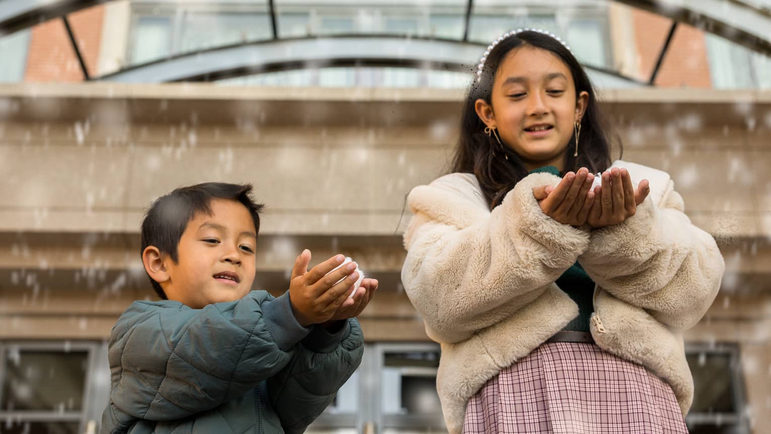 Two kids play with faux snow falling from the ceiling of a hotel entrance