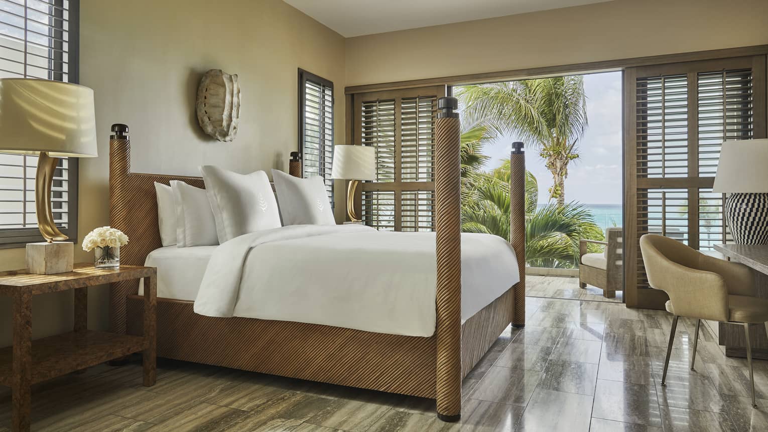 Bright bedroom with four-poster bed, wood accents and balcony view of palm trees and ocean.