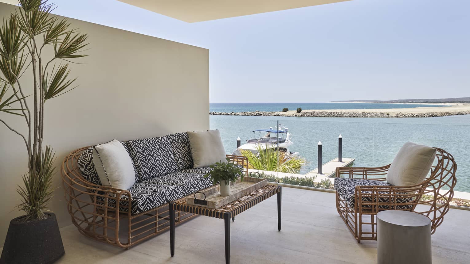 Balcony with whicker sofa and chair, table, plant, marina view