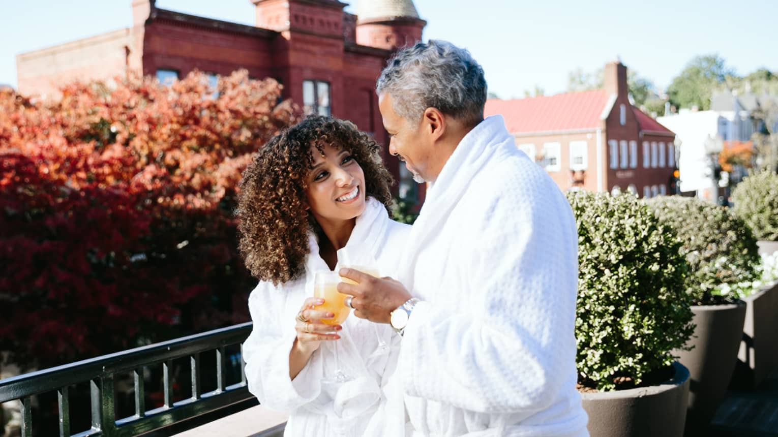 Two guests wearing robes and standing on a balcony holding drinking glasses