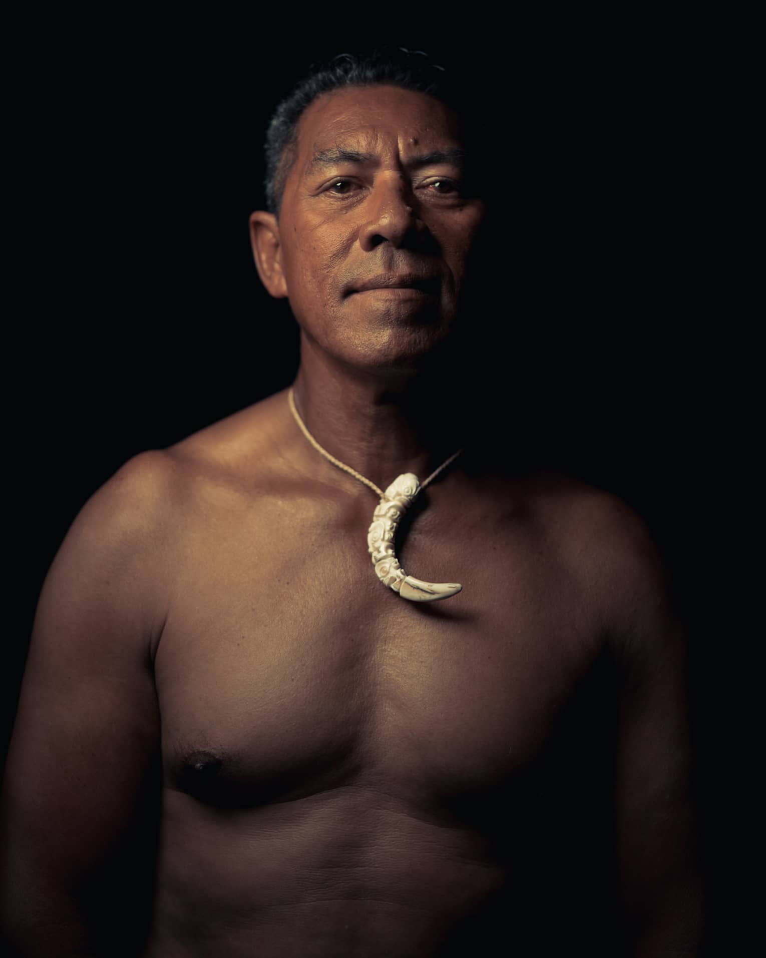 Person wearing a crescent-shaped necklace, standing against a dark background