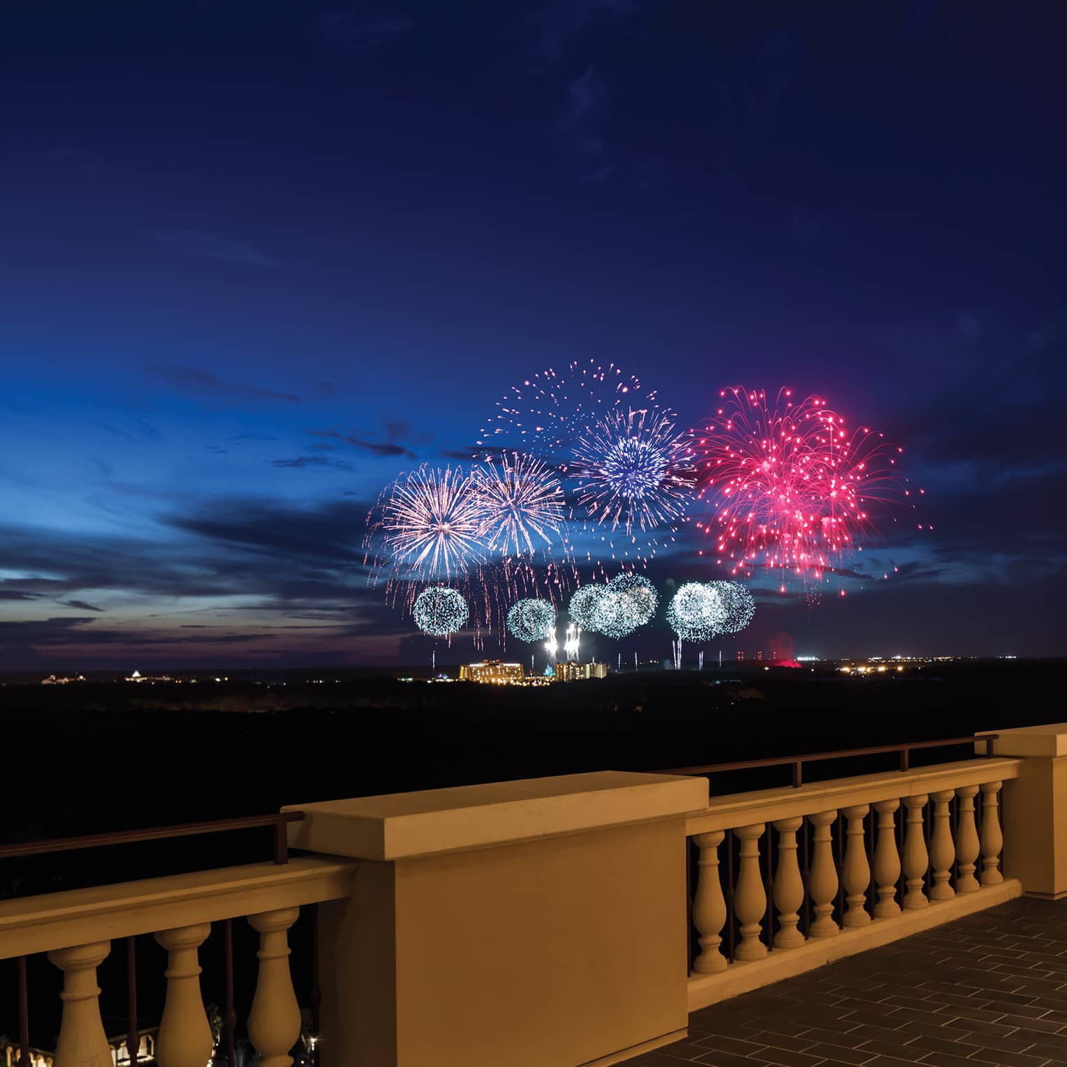 The terrace of a restaurant with tables and people watching fireworks in the distance.