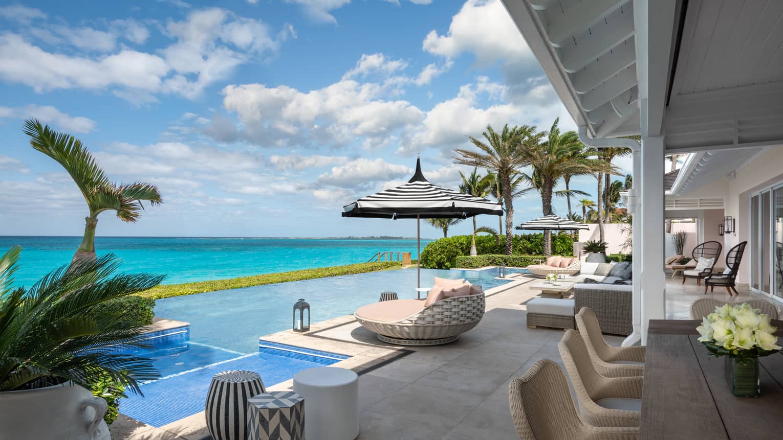 Beachfront villa residence terrace with private infinity pool, sun loungers, and ocean view under a bright blue sky