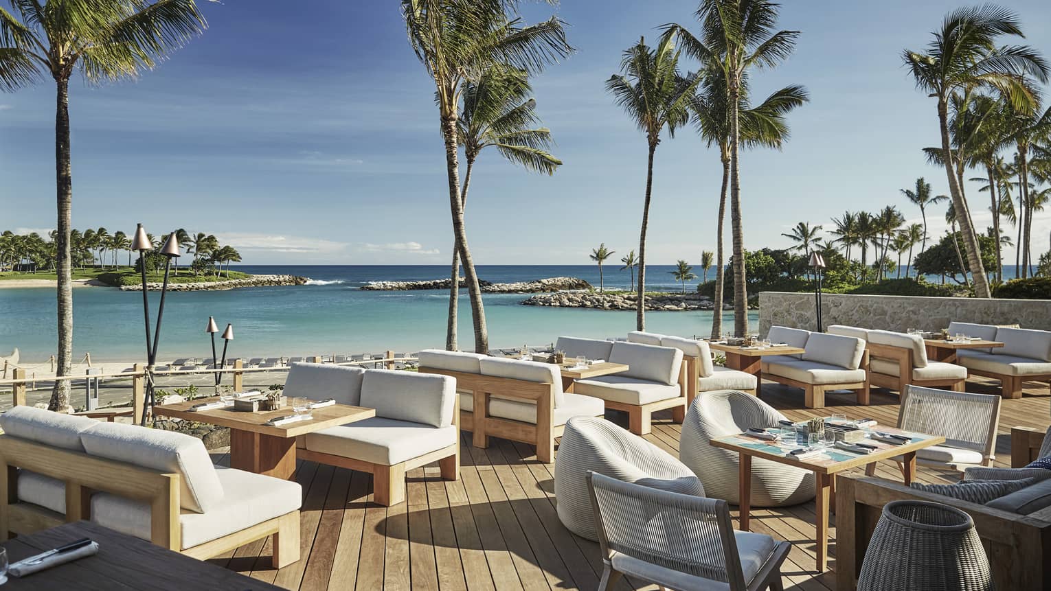 Plush white patio chairs around wood tables on sunny waterside Minas lounge