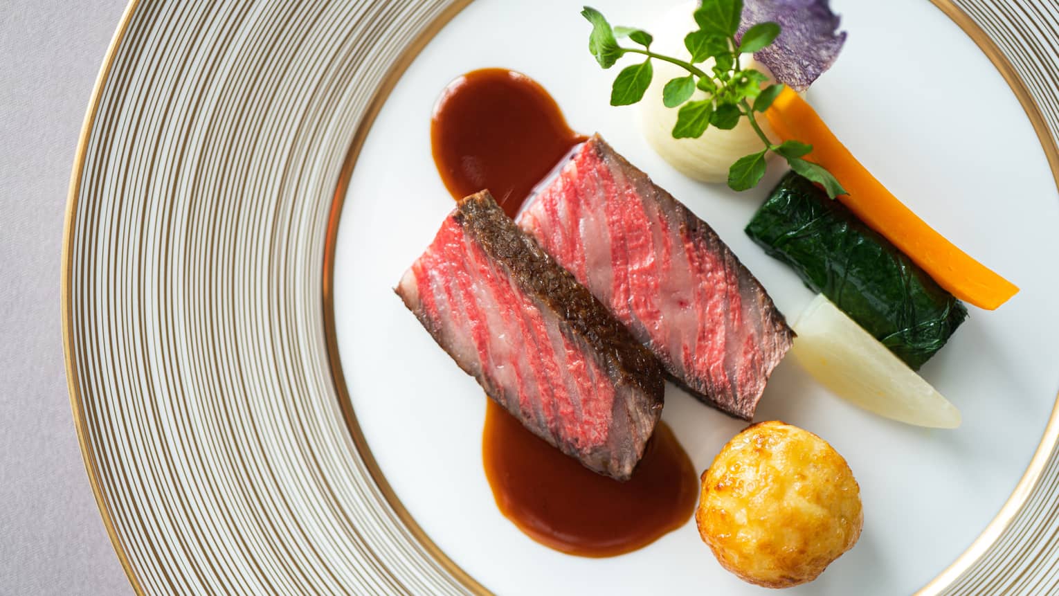 Aerial shot of grilled NY strip steak (rare) with demi-glace and vegetable garnishes