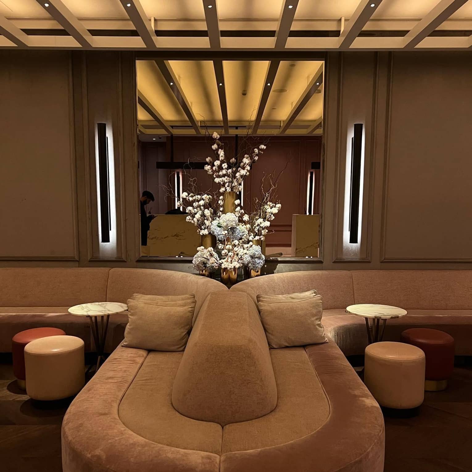 Velvet lounge seating at Marcus Restaurant and Terrace, with circular tables and stools, in front of a mirrored wall adorned with a large, white floral arrangement
