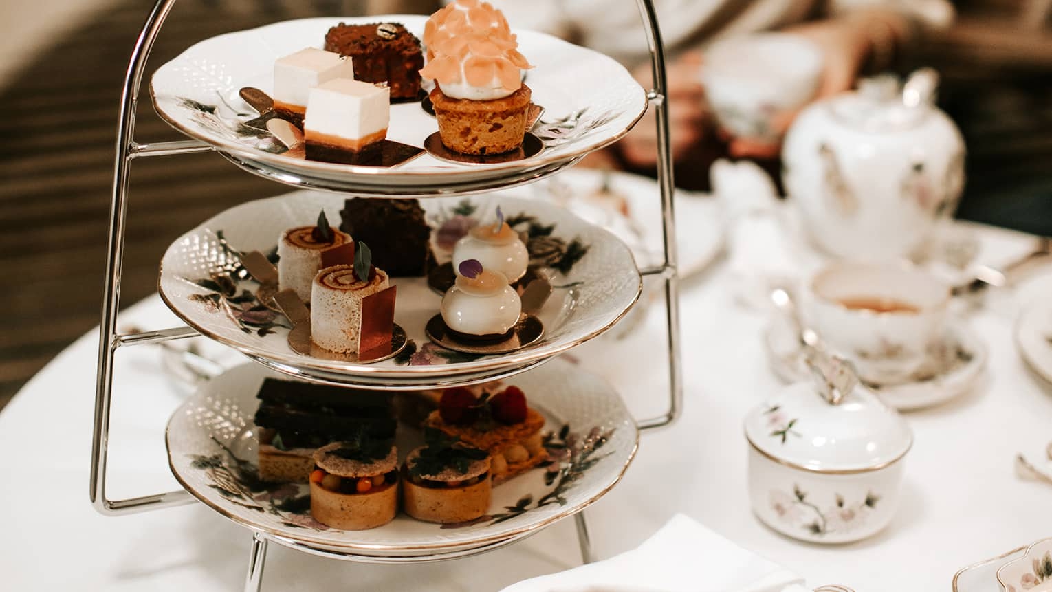 A woman sits at table with three-tiered Afternoon Tea tray
