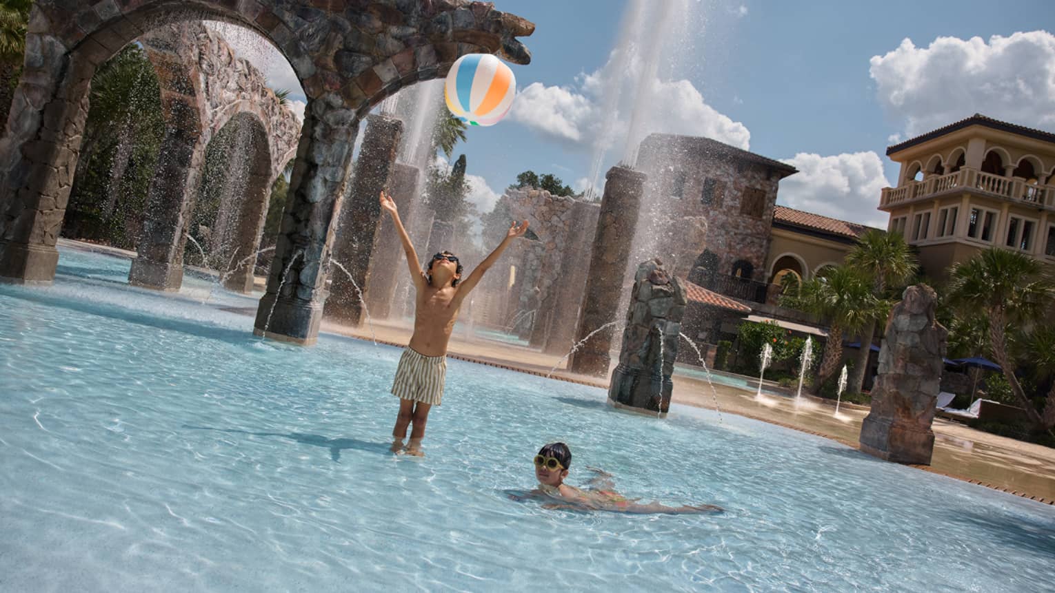 Two young guests wearing swimsuits and throwing a beach ball at the pool.