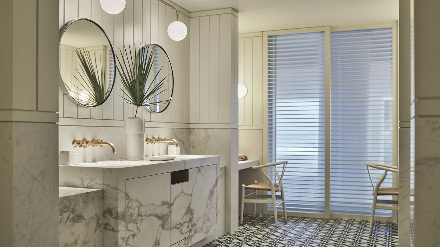 Luxury bathroom with marble double sinks, round mirrors, brass fixtures, patterned tile flooring and a seating area with soft lighting