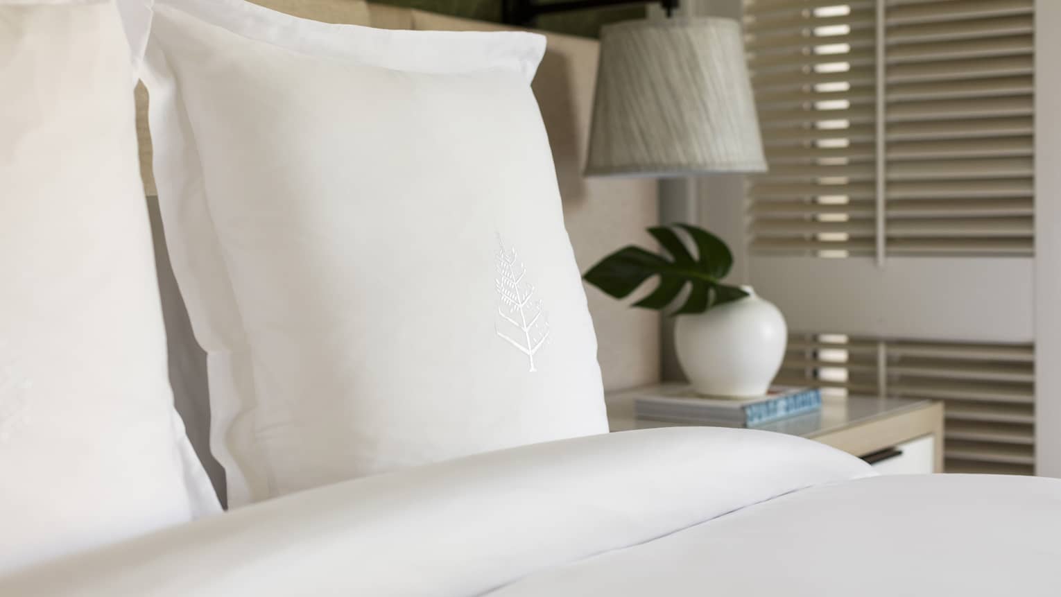 Bed with white sheets and pillow with Four Seasons logo embroidered on it