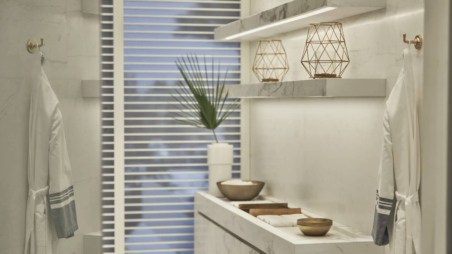 Spa interior with white marble shelves, decorative bowls, geometric lanterns and robes hanging on gold hooks