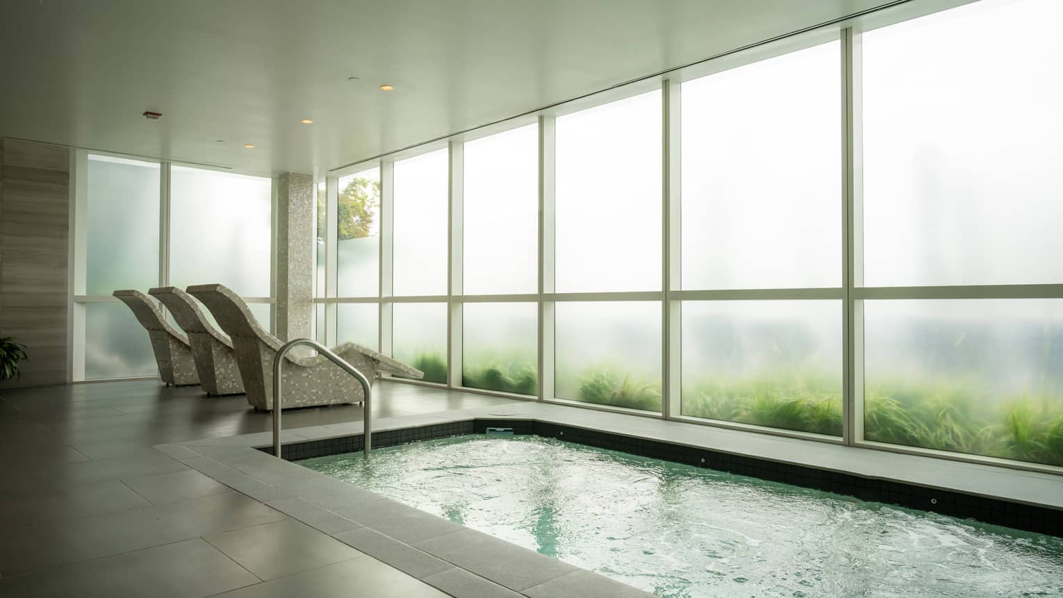 A room with three lounge chairs and a pool and floor-to-ceiling windows