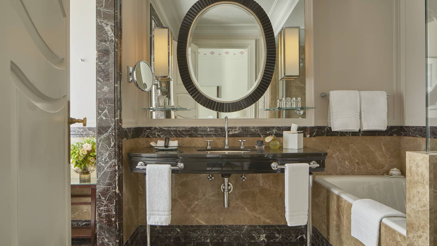 Elegant hotel bathroom with oval mirror, marble vanity and soaking tub