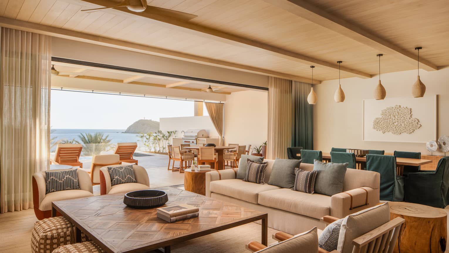 Stylish great room of a sea-view luxury residence, with a large square coffee table, sofa, arm chairs, and large dining table