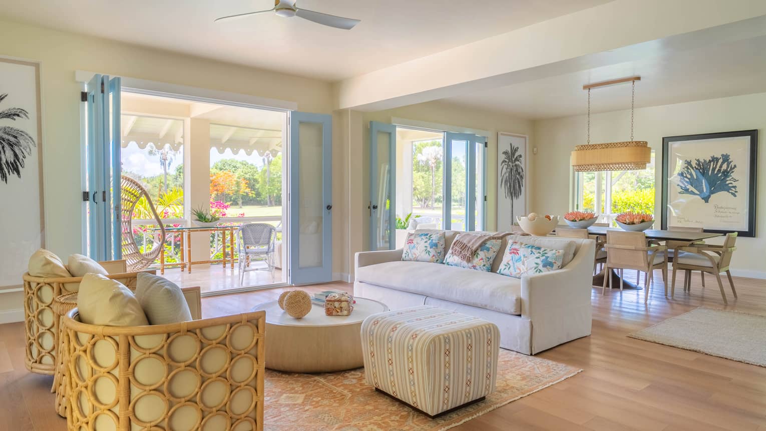 Airy living room with beige sofa, rattan arm chairs, wooden floors and light blue doors leading to tropical terrace