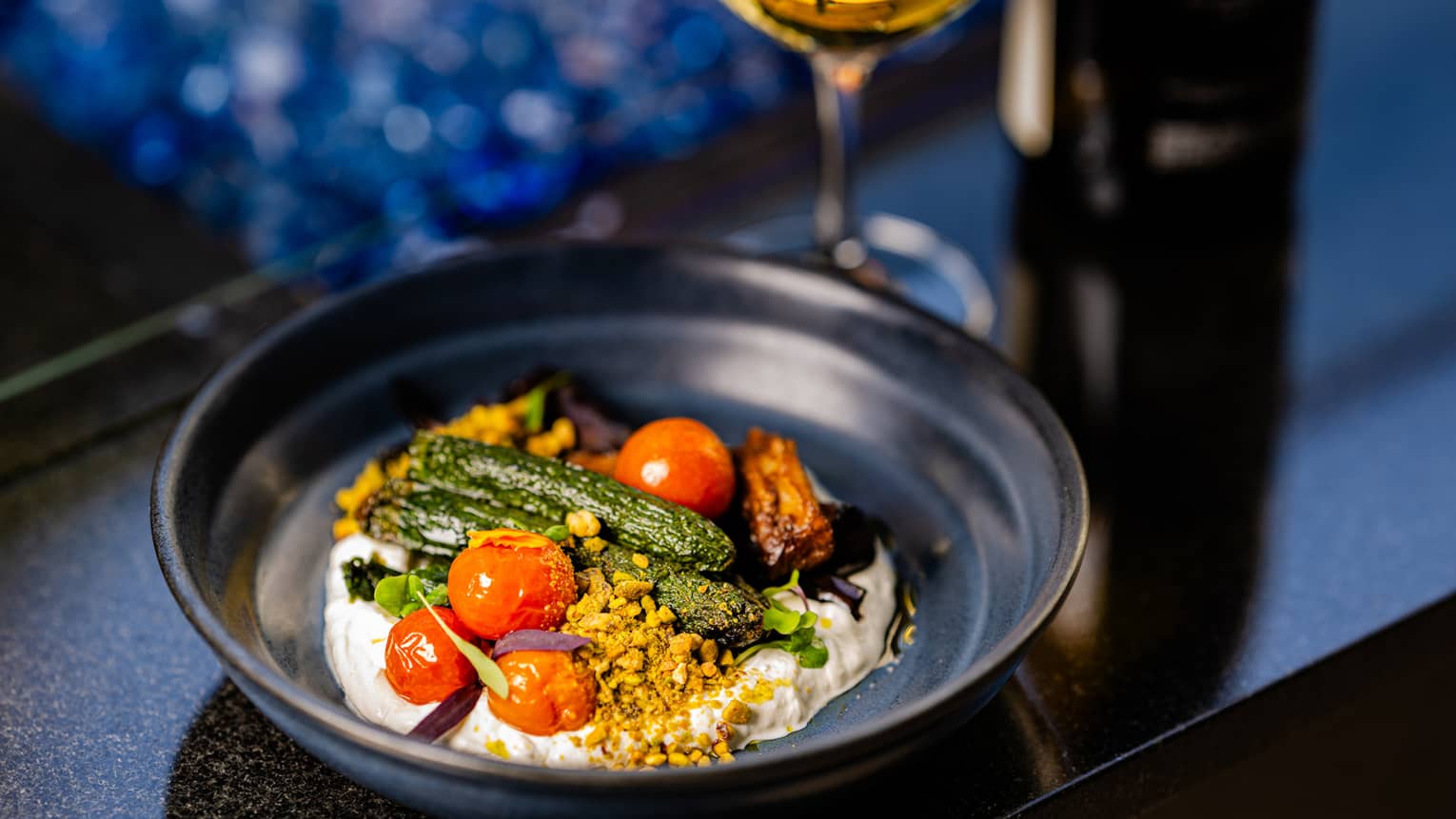 A food dish with tomatoes and green vegetables and a wine glass beside the plate