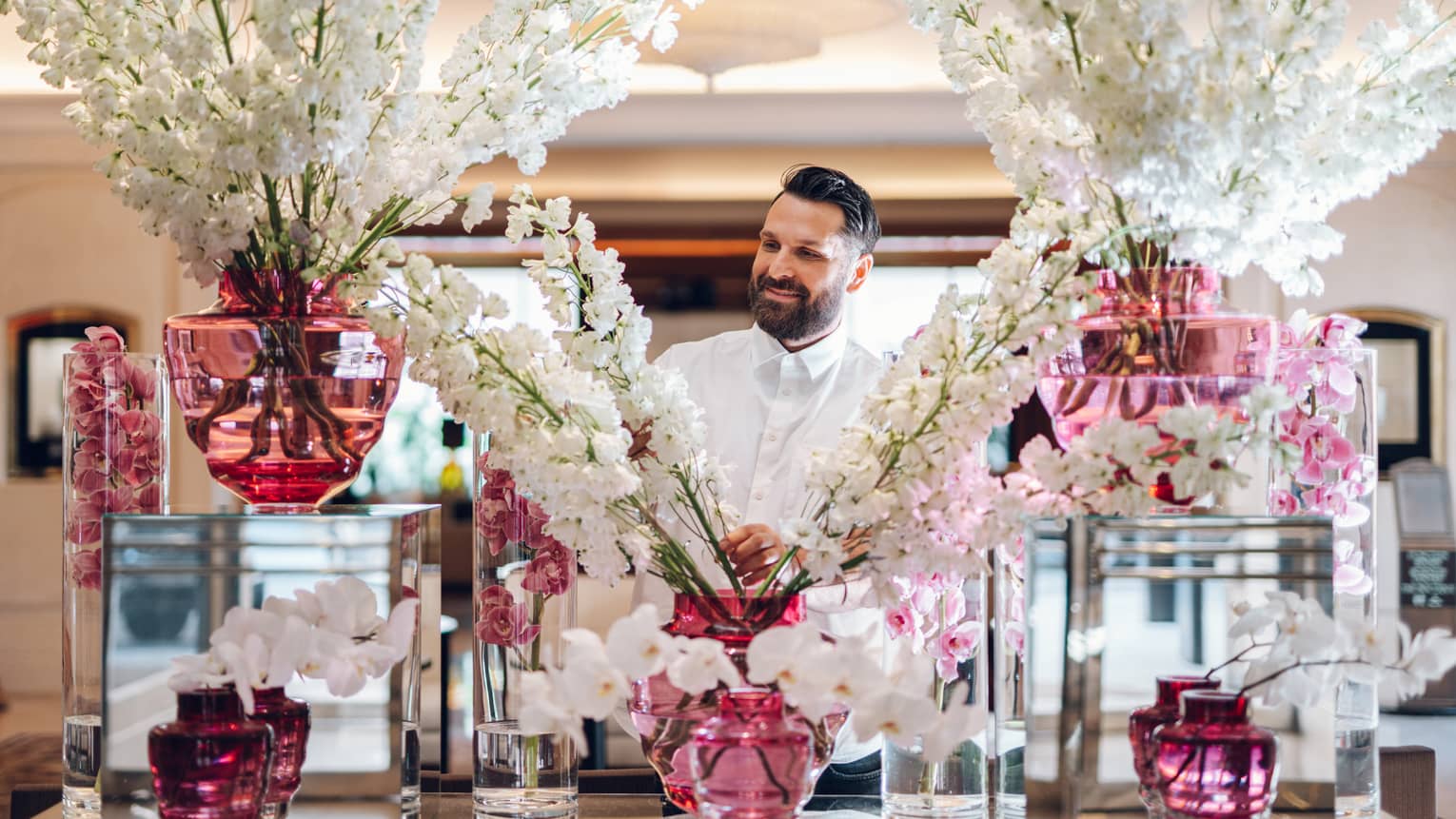 Floral designer standing behind large display of white flower sprays in assorted pink vases