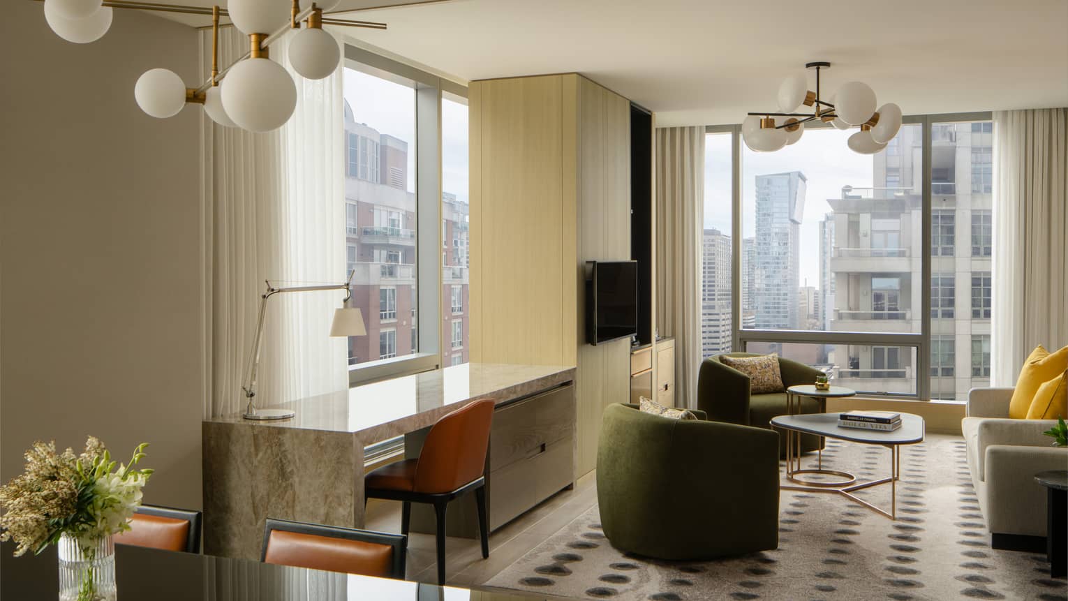 Open-concept living space with green armchairs, a beige sofa, TV and marble console table beside floor-to-ceiling windows offering city views