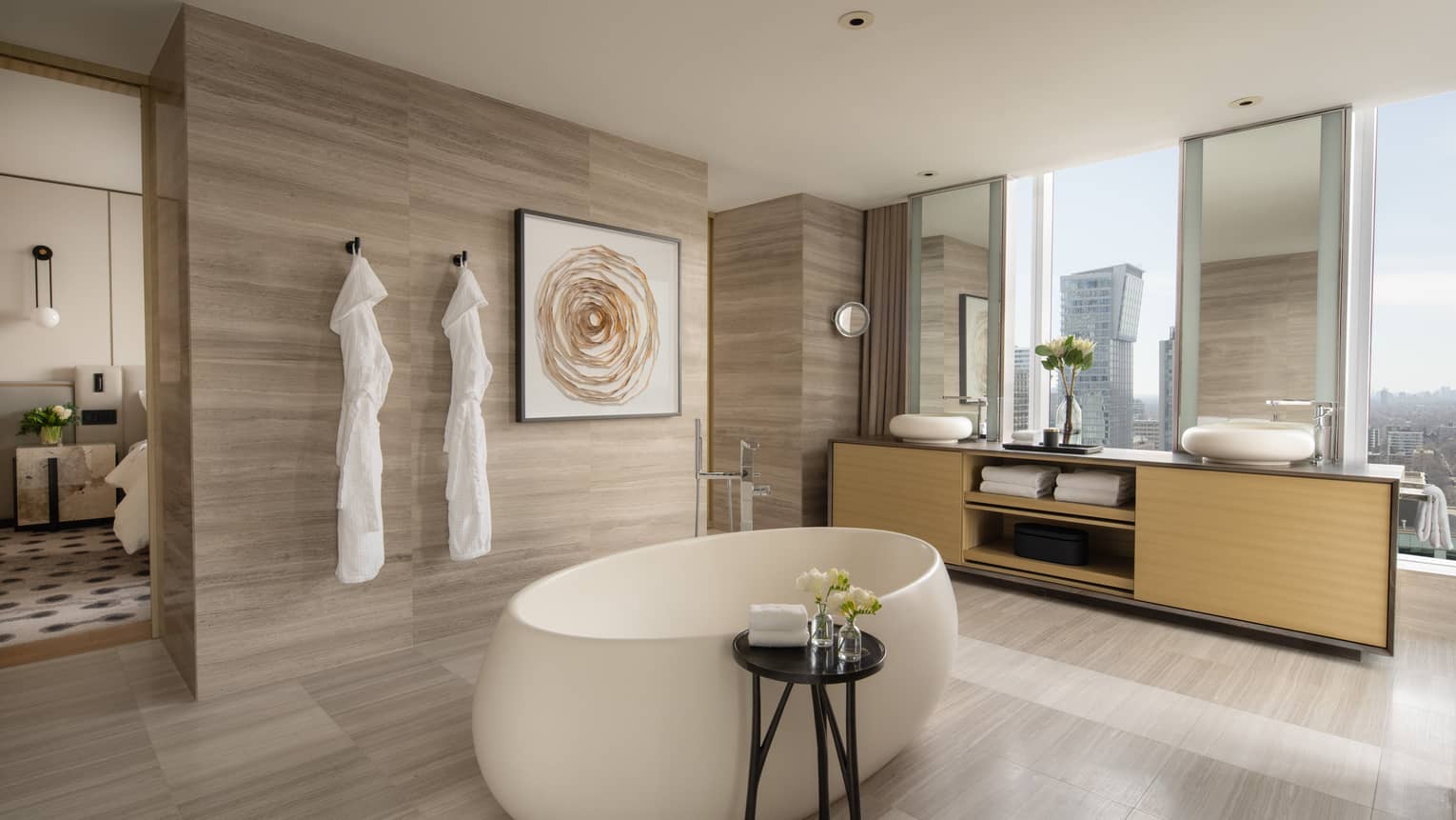 Royal suite bathroom with floor-to-ceiling windows, an oval soaking tub and double sinks, featuring natural wood tones