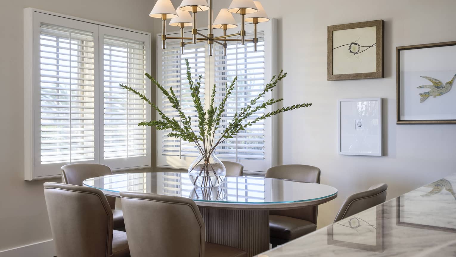 Elegant dining room in villa, with six chairs, large floral arrangement, and white shutter blinds on windows