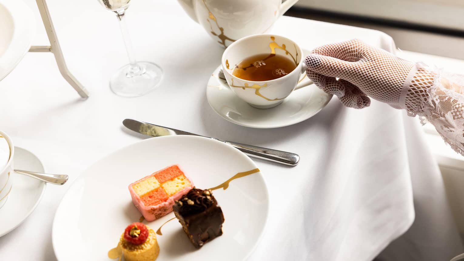 A woman picking up a cup a tea with a plate of small treats next to it.