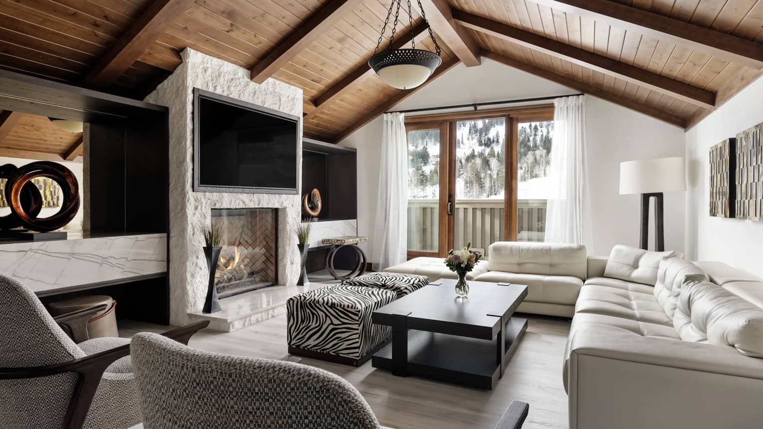 Mountain chic living room with large sofa, two grey arm chairs, vaulted wooden ceiling, stone hearth and TV