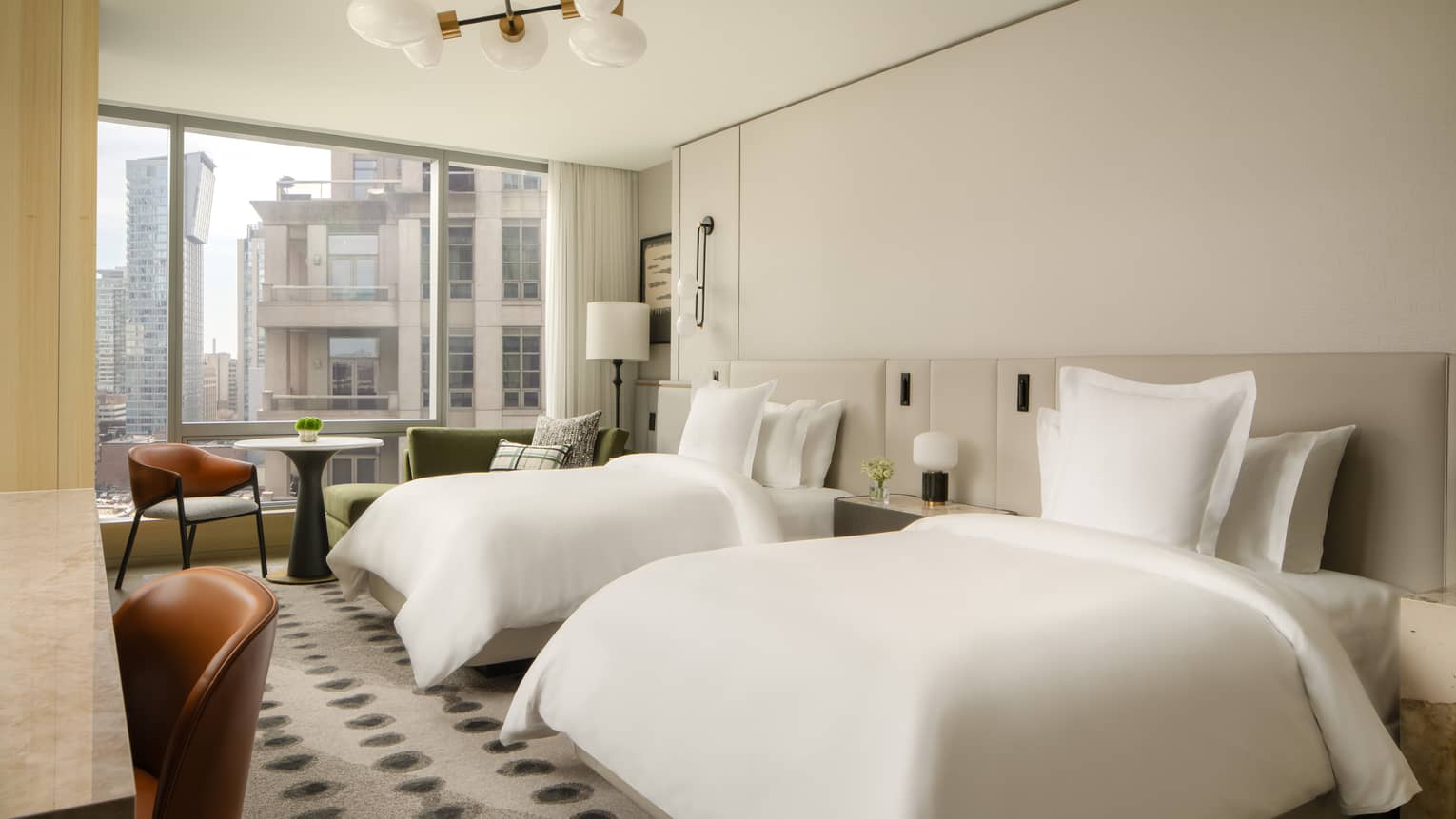 Luxury hotel room with two double beds, floor-to-ceiling windows with city views, and a cozy seating area in a neutral, elegant décor
