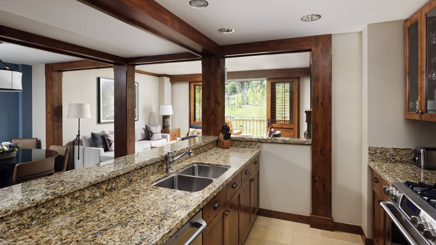 Kitchen with granite countertops, wooden cabinetry, and a sink overlooking a bright living area with access to an outdoor balcony