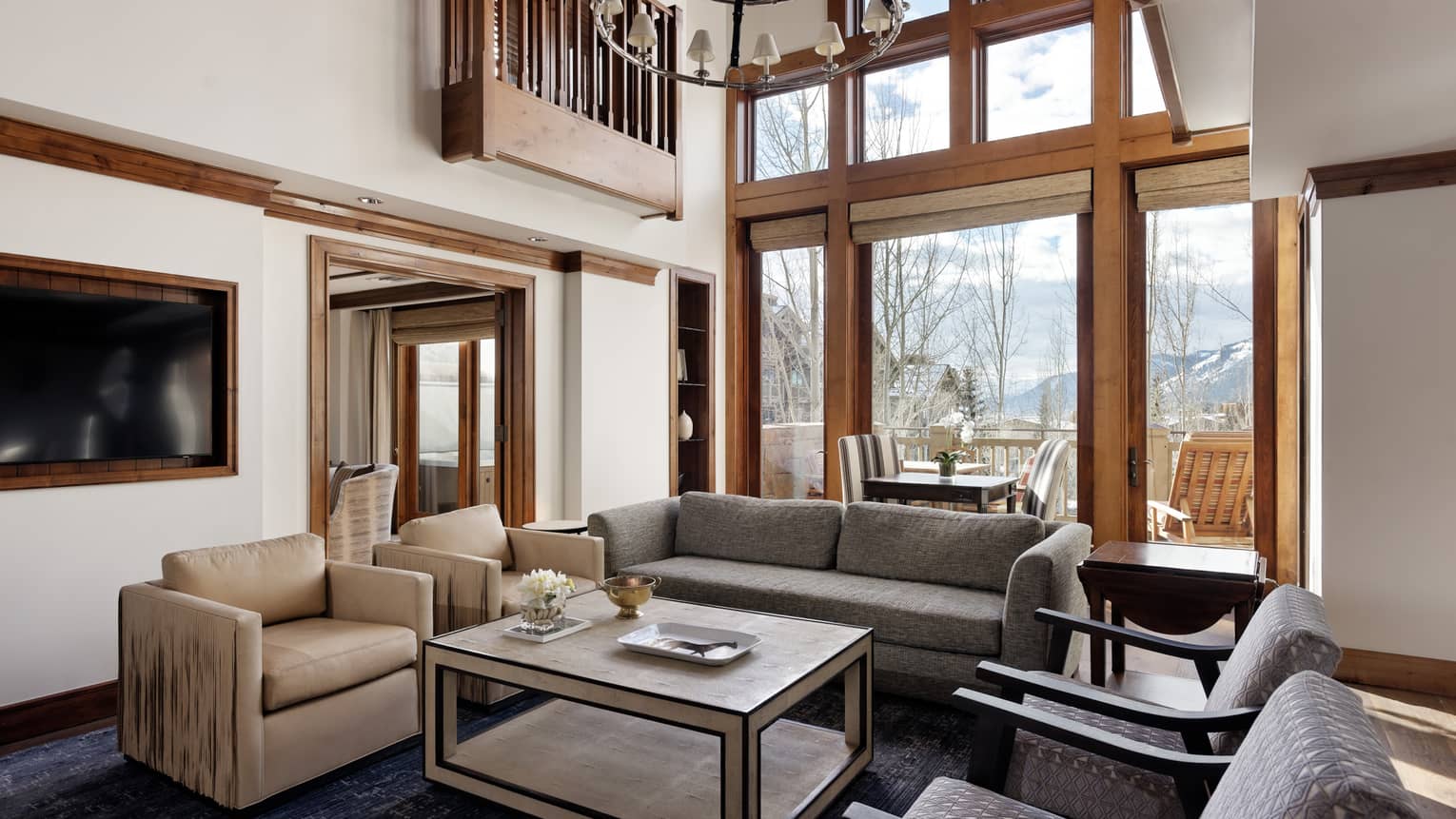 Living room with high ceilings, beige and grey patterned armchairs, grey sofa, coffee table and outdoor balcony with mountain view