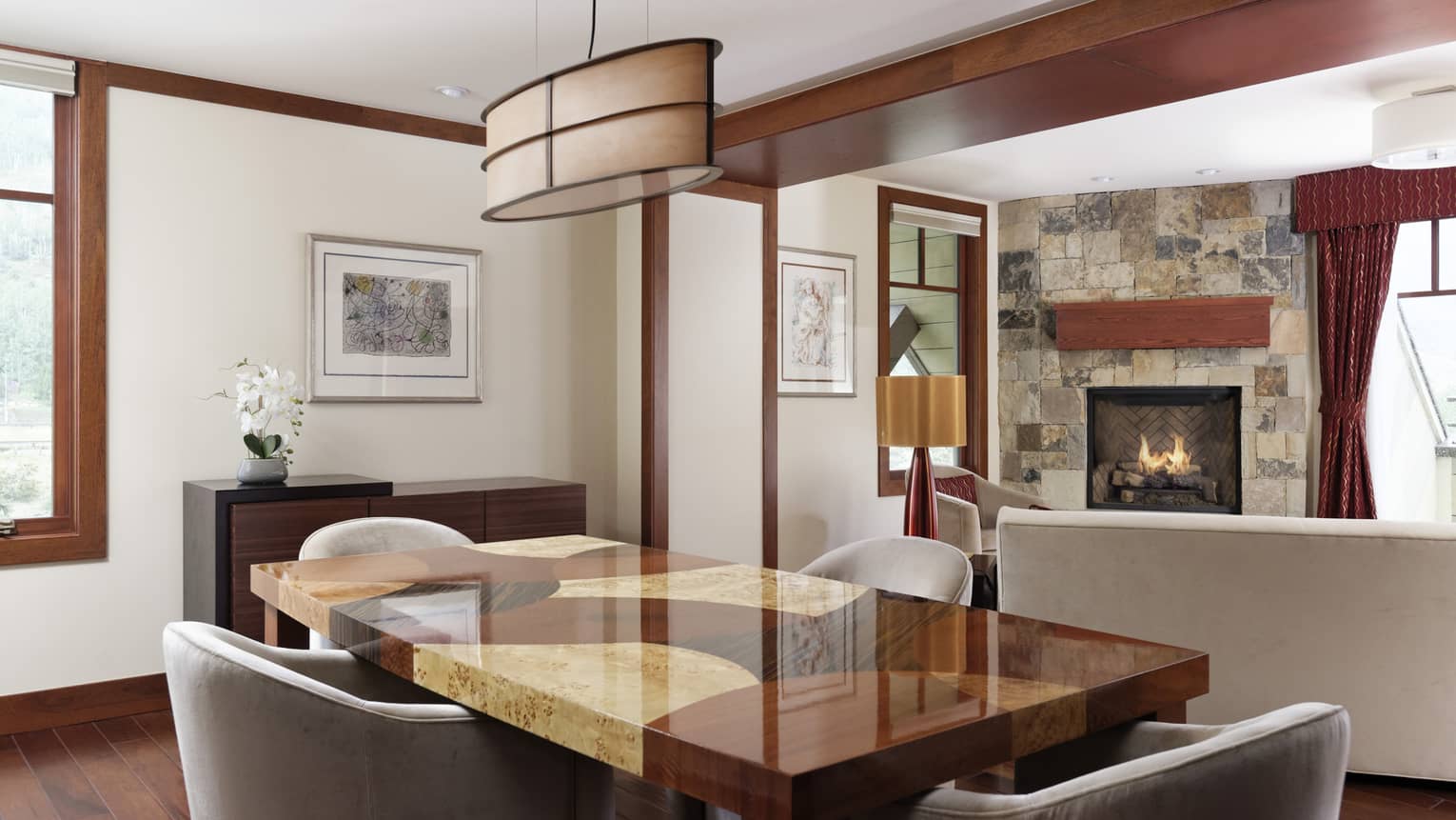 Dining table made of multiple shades of wood, grey chairs, stone hearth in the background