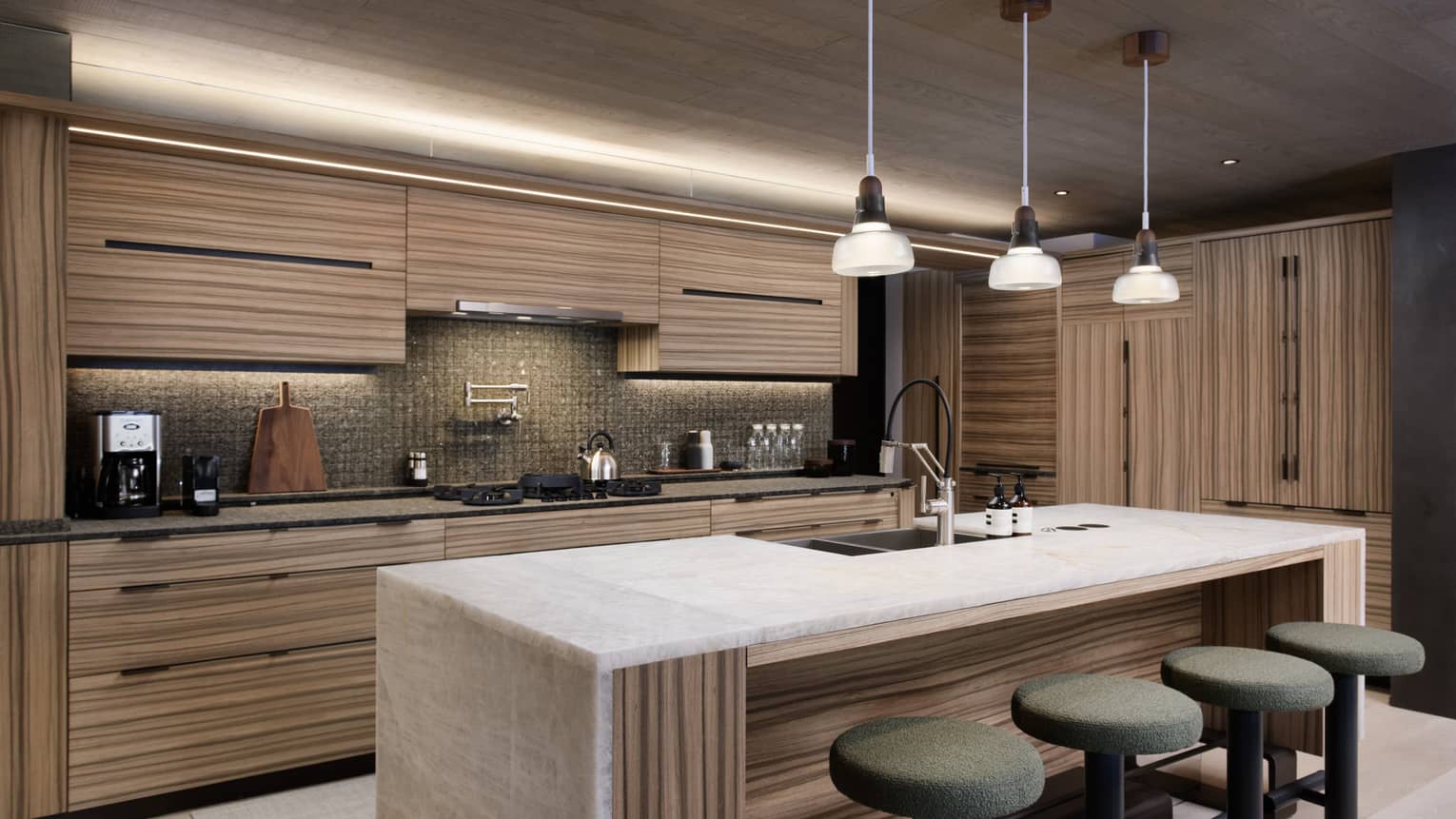 Contemporary kitchen with light wood cupboards, matching island, three pendant lights and four sage-green stools