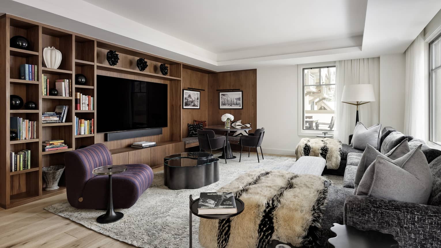 Contemporary living room of a private residence rental, featuring a grey sofa, plum-coloured arm chair and built-in media centre